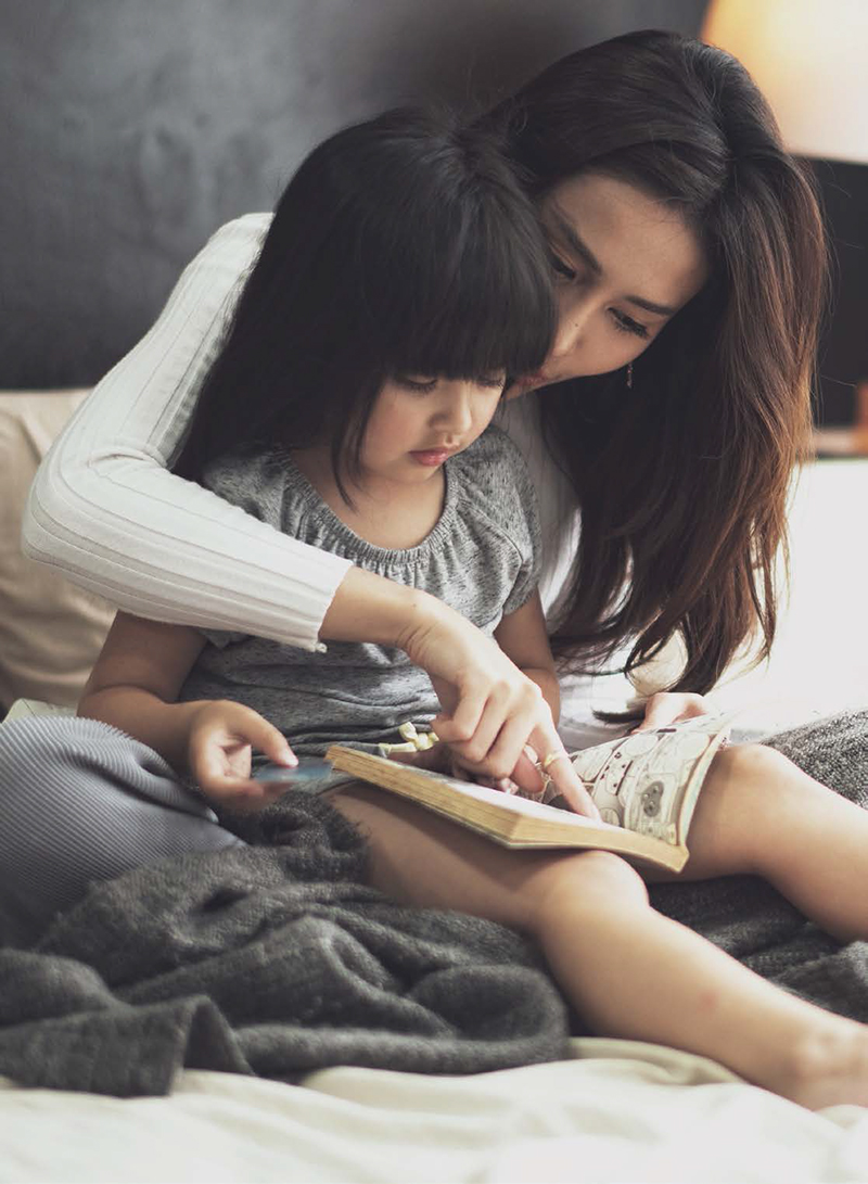 Love of young mother and daughter. Teaching reading a homework or book on the bed at home. mother and daughter look at the book feel good